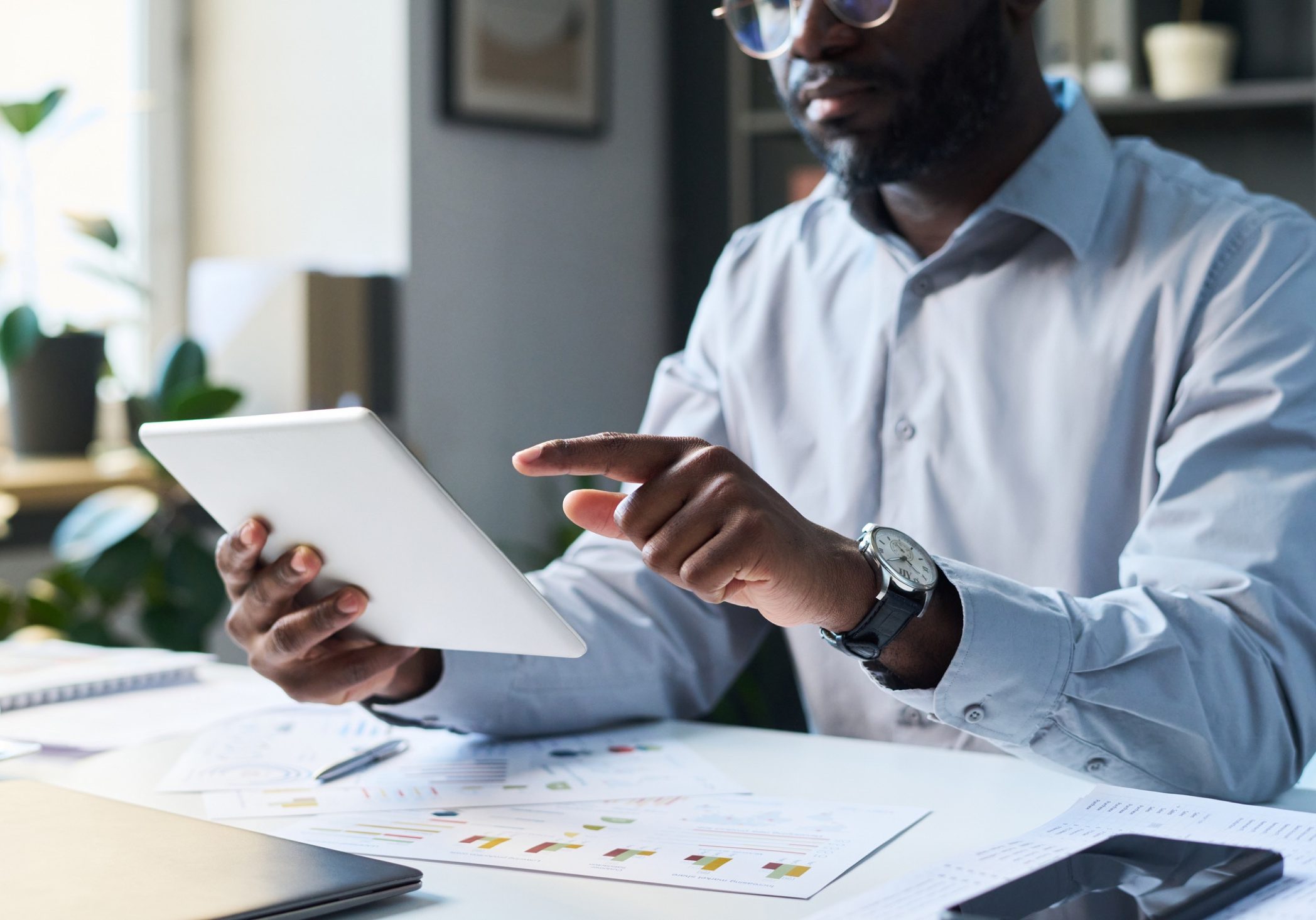 Medium closeup of modern black male company director sitting in office, using digital tablet during workday