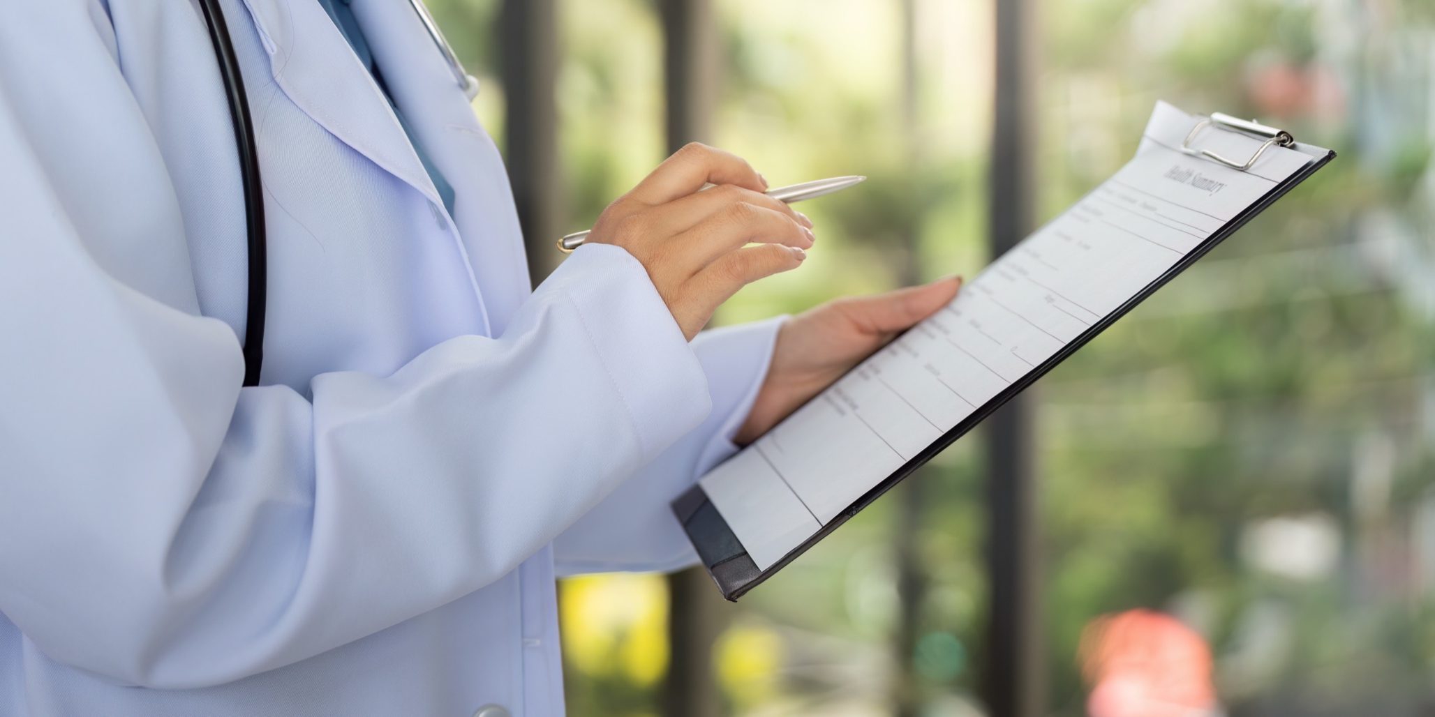 A doctor in a white coat checks a patient's chart while holding a pen, emphasizing patient care and attention to detail.